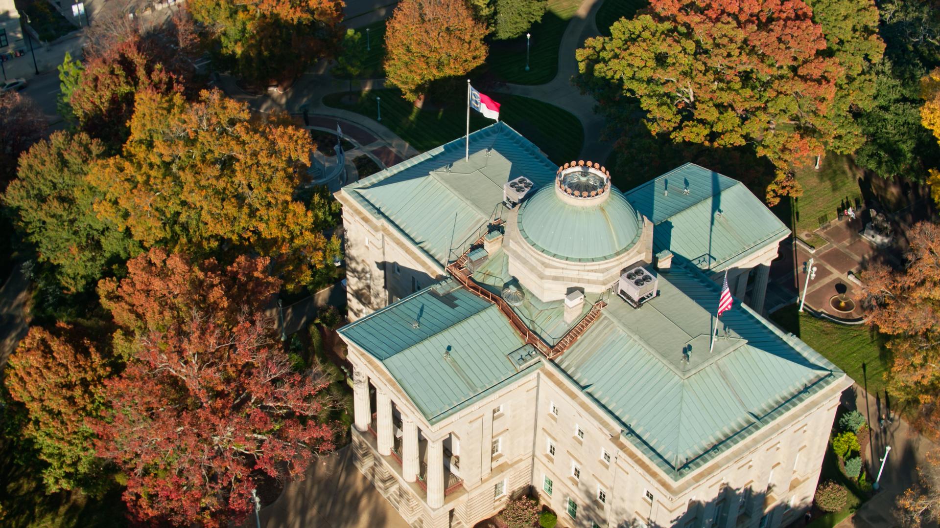 North Carolina and US Flags Flying Over State Capitol Building in Raleigh - Aerial